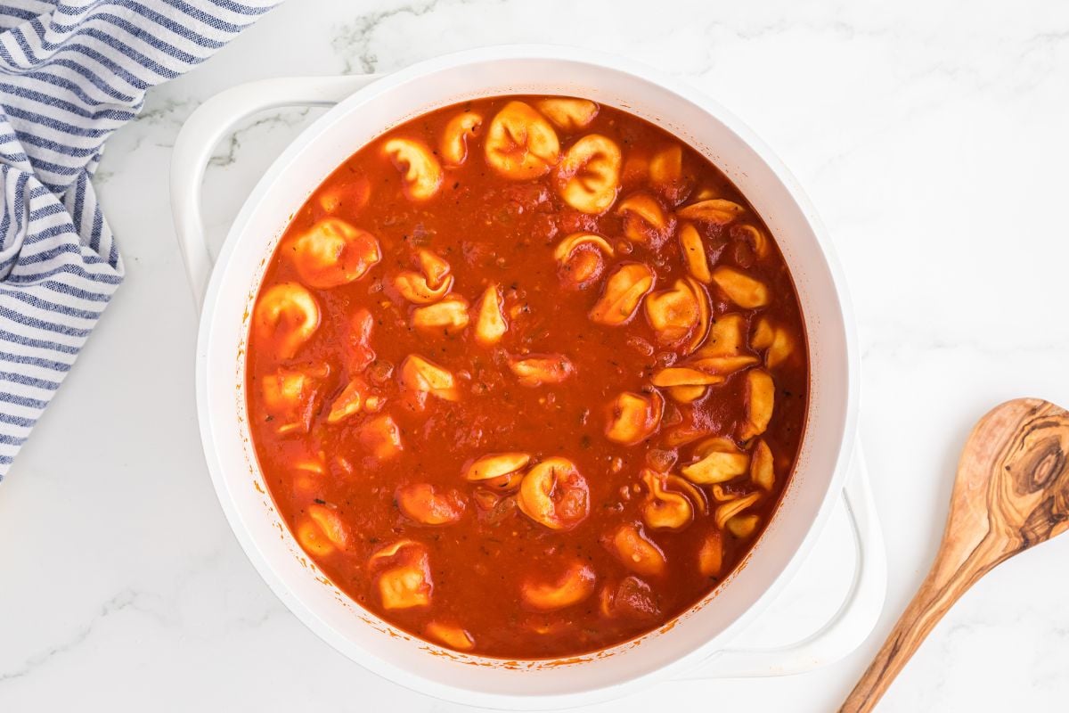 tortellini added to red broth in pot.