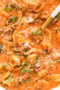 A close-up shot of a bowl of creamy tortellini soup garnished with parmesan and basil, ready to be served.