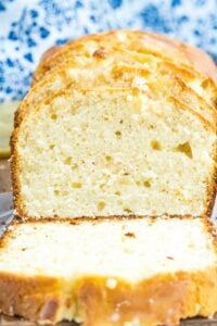 Sliced lemon bread on a plate, with a moist crumb and golden crust, showcasing the texture and lemon zest speckled within.