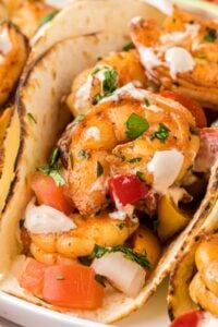 Close-up of shrimp fajitas inside charred tortillas, focusing on the texture of the shrimp and the garnishes, ready to be served.