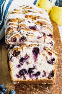 sliced blueberry quick bread with glaze on wooden board.