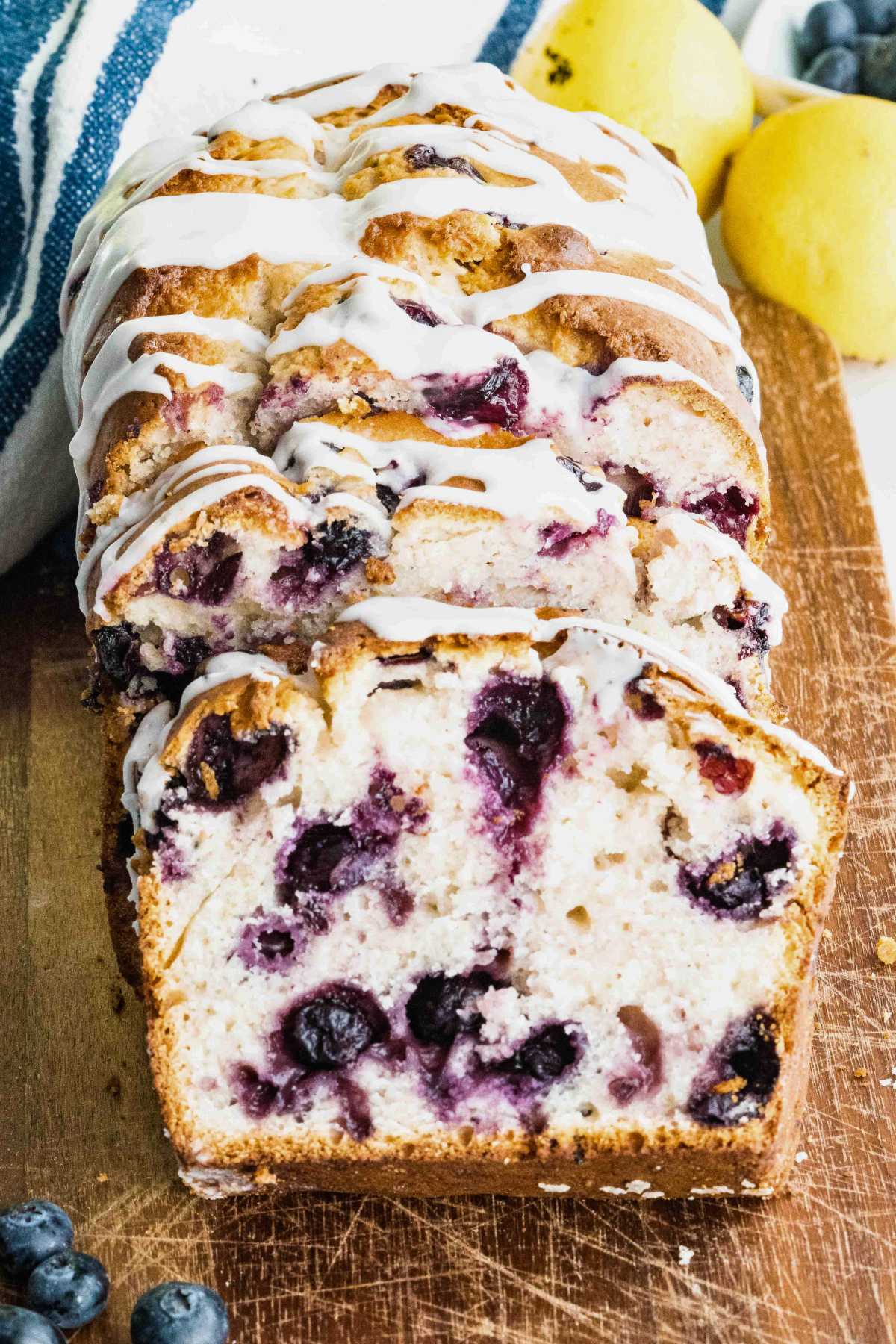 sliced blueberry quick bread with glaze on wooden board.