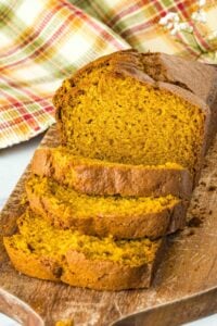 a baked loaf of sourdough pumpkin bread on a cutting board, with a few slices cut.
