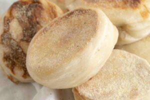 A stack of cooked sourdough English muffins showing the textured side.