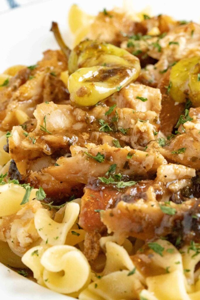 Close-up of Crockpot Mississippi Chicken mixed with egg noodles, showing the combination of shredded chicken, spices, and pepperoncini.
