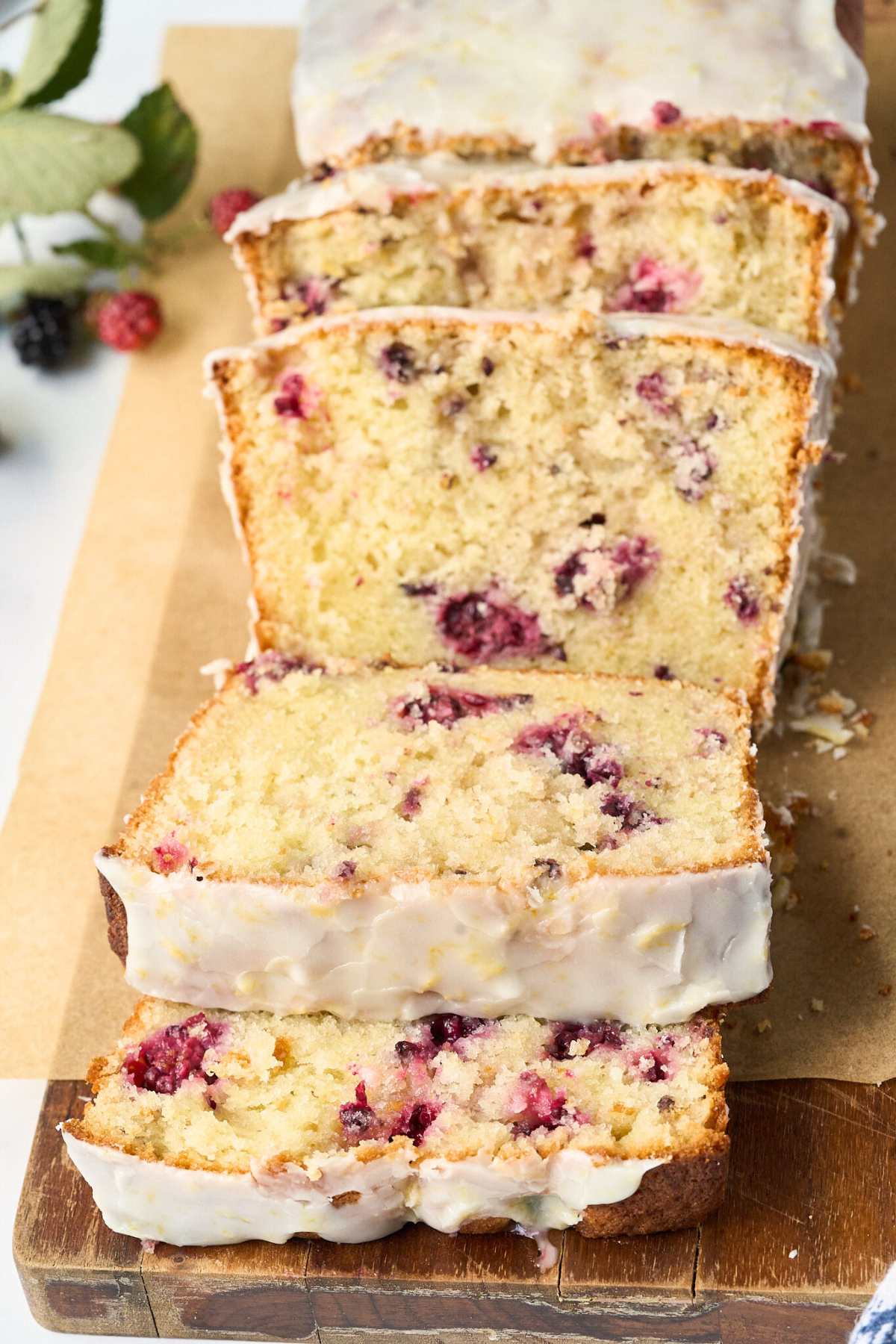 Sliced blackberry lemon pound cake with white glaze on cutting board.