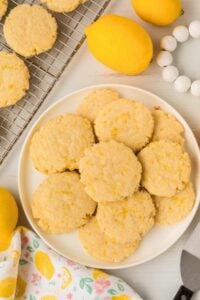lemon sugar cookies on plate with tea towel and lemon nearby.