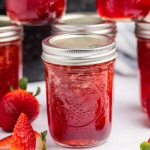 jar of strawberry preserves with other jars in background and strawberries beside.