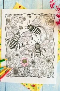 An in-progress coloring page with bees and flowers is displayed, partially colored with pastel hues, accompanied by a set of colored pencils, all atop a rustic wooden surface