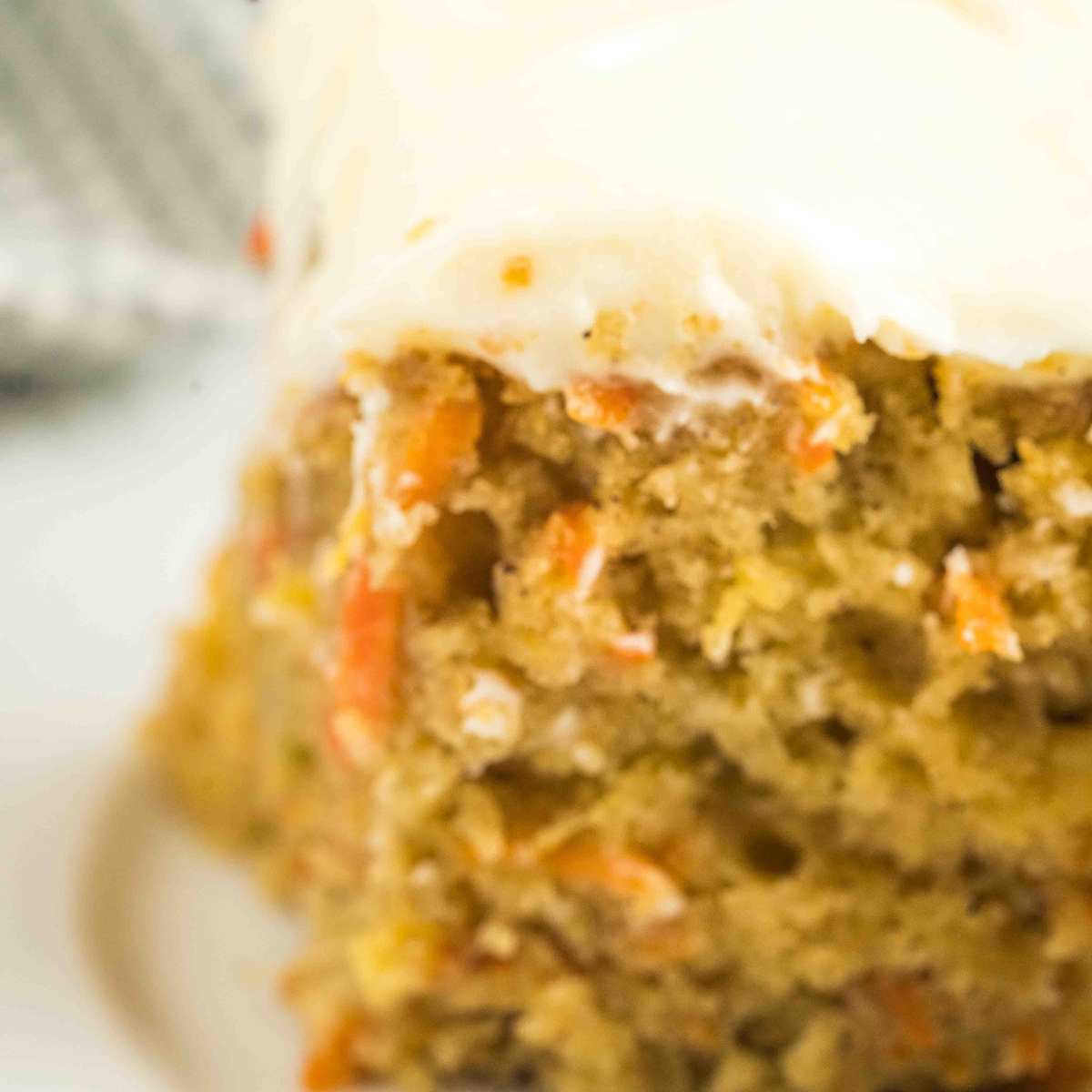 Sourdough carrot cake with cream cheese frosting, in soft focus, creating a dreamy effect that emphasizes the texture of the cake and the creamy frosting on a white plate with a grey cloth in the background.