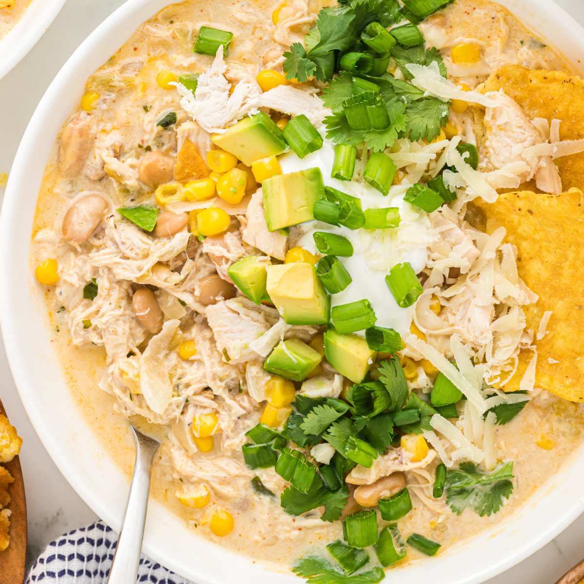 bowl of white chicken chili garnished with avocado, shredded cheese, green onions, and cilantro.
