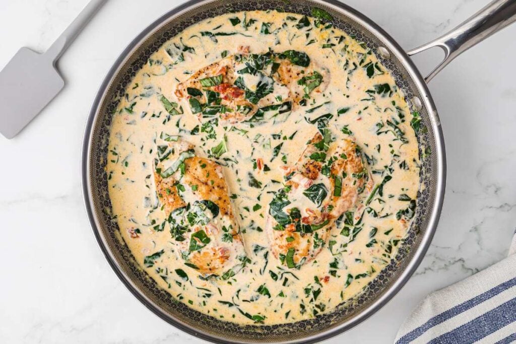 Skillet with Tuscan chicken breasts in a creamy sauce garnished with chopped spinach, viewed from an overhead angle.