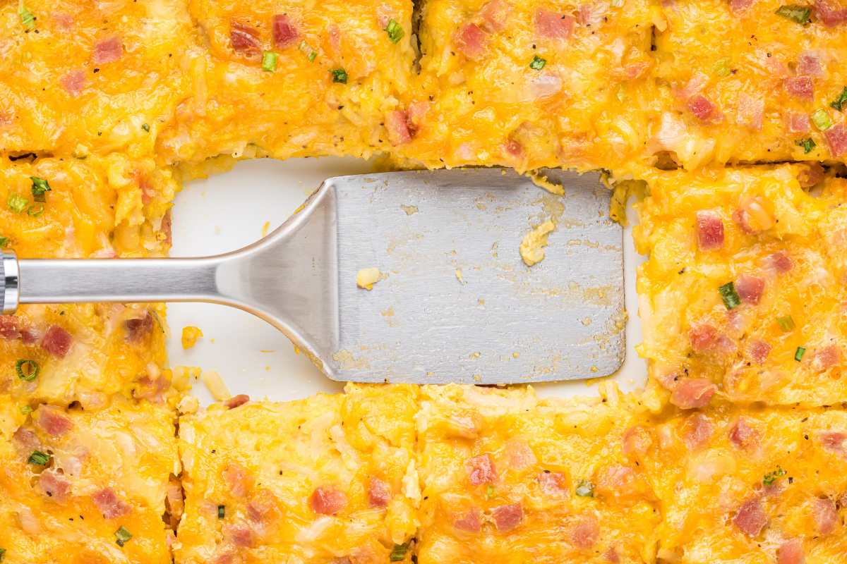 The casserole with a portion served, revealing the layers of egg, cheese, and ham, with a serving spatula inside the dish.
