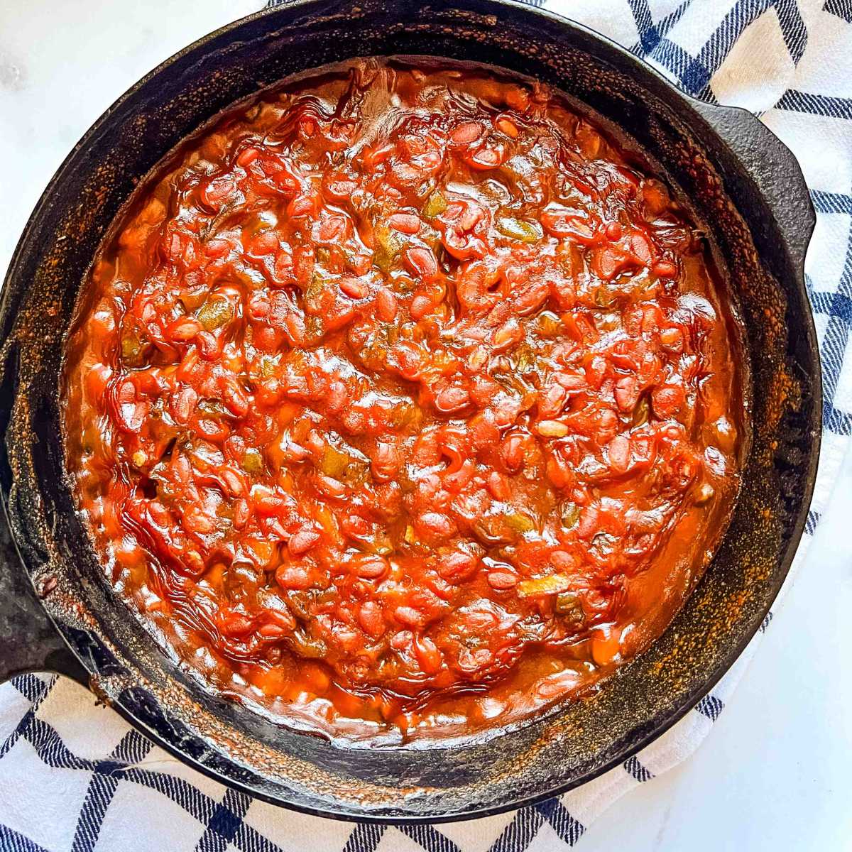 baked beans in cast iron skillet on top of towel on counter.