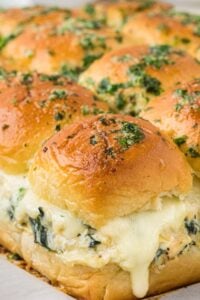 A tray of chicken spinach artichoke sliders with a golden crust sprinkled with herbs, highlighting the layers of melted cheese and creamy spinach artichoke filling
