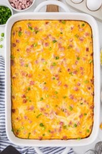 A freshly baked Ham and Hashbrown Breakfast Casserole in a white baking dish, topped with melted cheese and garnished with green onions, ready to be served.