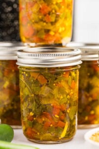 A row of glass jars filled with freshly canned jalapeño relish, ready for storage, showing the mixture's rich green and red colors.