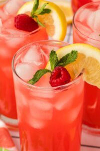 finished Lemonade in a glass pitcher, garnished with lemon slices and raspberries,