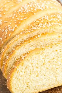 Angled view of a sliced soft Italian bread loaf with sesame seeds, showcasing the airy interior and golden crust.