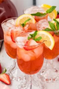 glasses of strawberry sweet tea filled with ice, garnished with lemon slices and mint leaves.