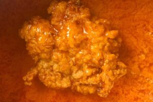 A close-up of a fried chicken tender being dipped in buffalo sauce, coated evenly with the spicy mixture.