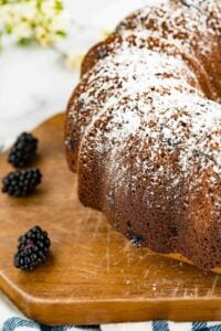 blackberry Bundt cake with powdered sugar on wooden board with blackberries beside.