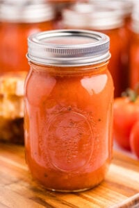 A sealed jar of homemade creamy tomato soup concentrate on a wooden cutting board, with fresh tomatoes in the background.