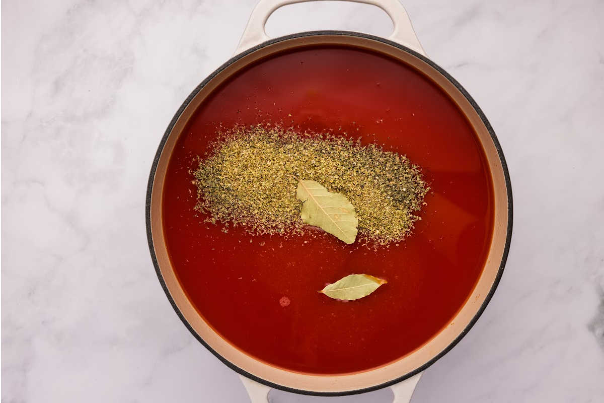 The tomato soup with added dried herbs and bay leaves in the cooking pot.