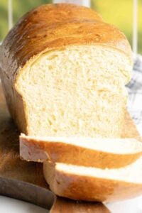 Golden-brown potato bread loaf on a cutting board, with two slices cut, showcasing its soft, fluffy texture.