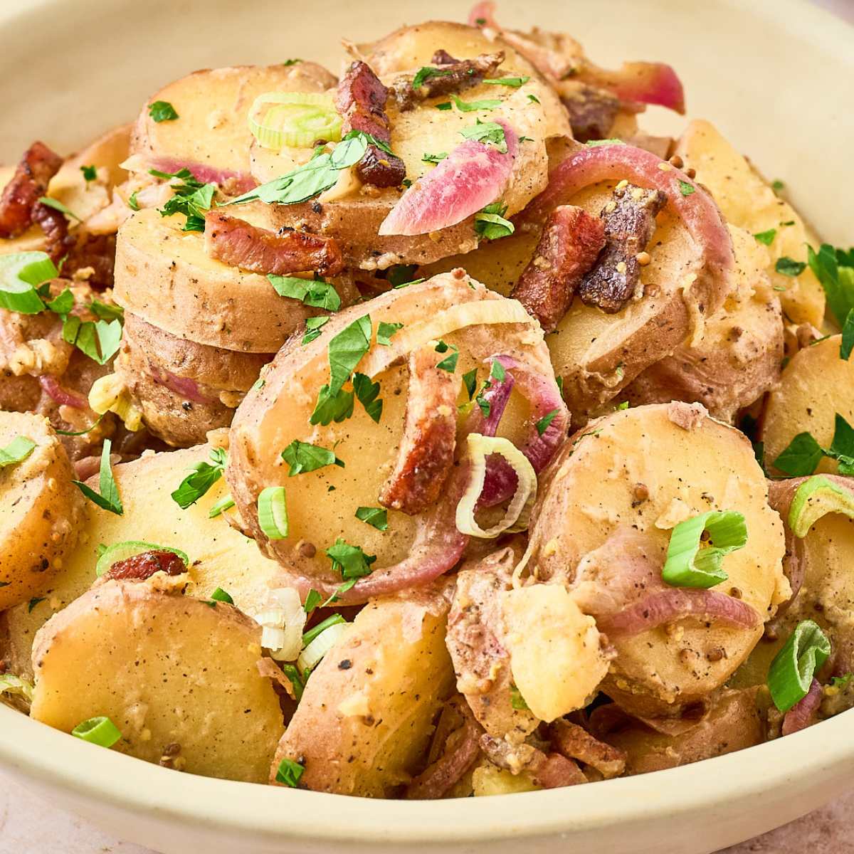 close up of potato salad with bacon and red onions, topped with parsley.