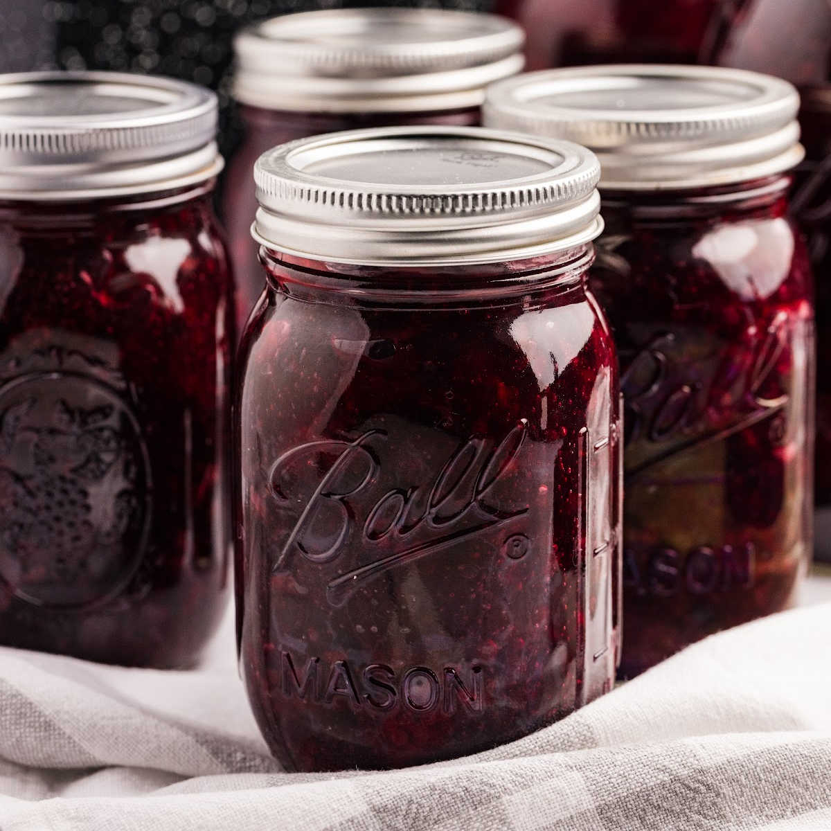 Jars of blackberry pie filling next to a bowl of fresh blackberries, ready for canning.