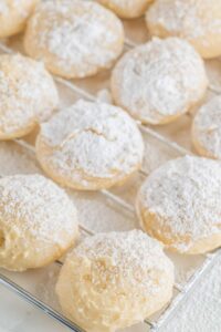 Freshly baked cream cheese cookies dusted with powdered sugar on a cooling rack.