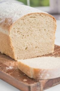 Close-up of a sliced loaf of Sourdough Farmhouse White Sandwich Bread on a wooden cutting board.