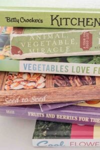 A collection of gardening books stacked together. Titles include 'Betty Crocker's Kitchen Gardens', 'Animal, Vegetable, Miracle' by Barbara Kingsolver, 'Vegetables Love Flowers' by Lisa Mason Ziegler, 'Seed to Seed' by Suzanne Ashworth, 'Fruits and Berries for the Home Garden' by Lewis Hill, and 'Cool Flowers' by Lisa Mason Ziegler.