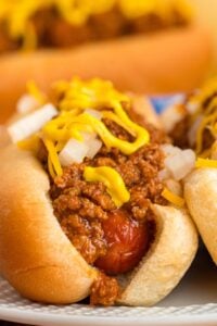 Close-up of a hot dog topped with chili, mustard, and chopped onions on a bun.
