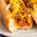 Close-up of a hot dog in a bun with chili, mustard, and chopped onions.