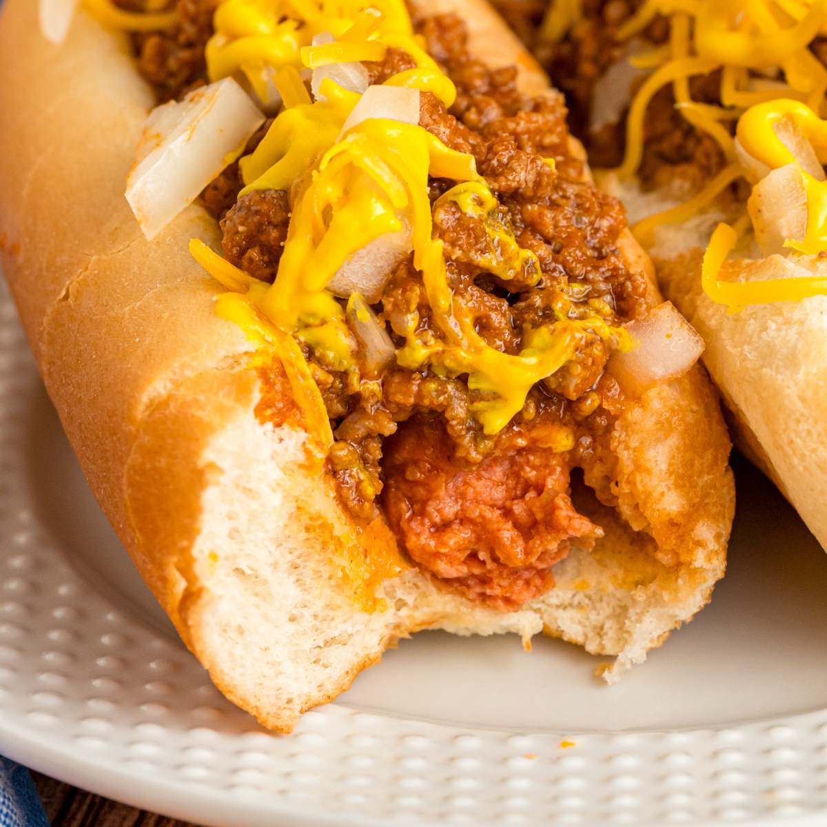 Close-up of a hot dog in a bun with chili, mustard, and chopped onions.