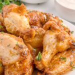 A plate of oven-baked chicken wings garnished with parsley, served alongside a bowl of ranch dressing.