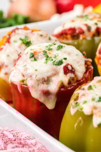 Stuffed bell peppers topped with melted mozzarella and garnished with chopped parsley in a white baking dish.