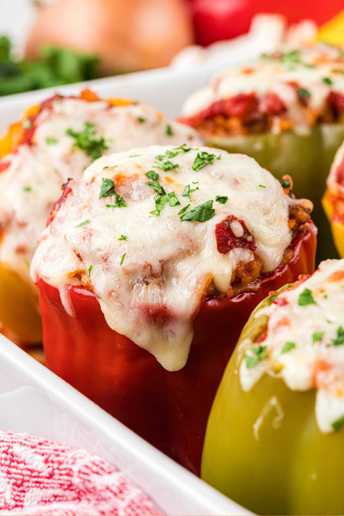 Stuffed bell peppers topped with melted mozzarella and garnished with chopped parsley in a white baking dish.