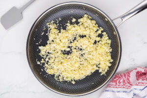 Diced onions and minced garlic sautéing in olive oil in a non-stick skillet, preparation for a flavorful base.