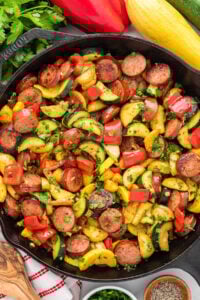 A colorful skillet meal with sausage, zucchini, yellow squash, red peppers, and chopped parsley.