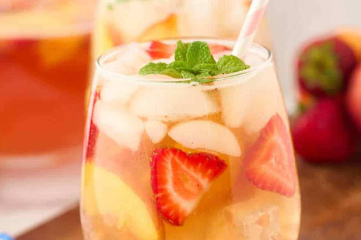 A glass of strawberry peach sangria filled with ice, garnished with slices of fresh strawberries, peaches, and a sprig of mint.