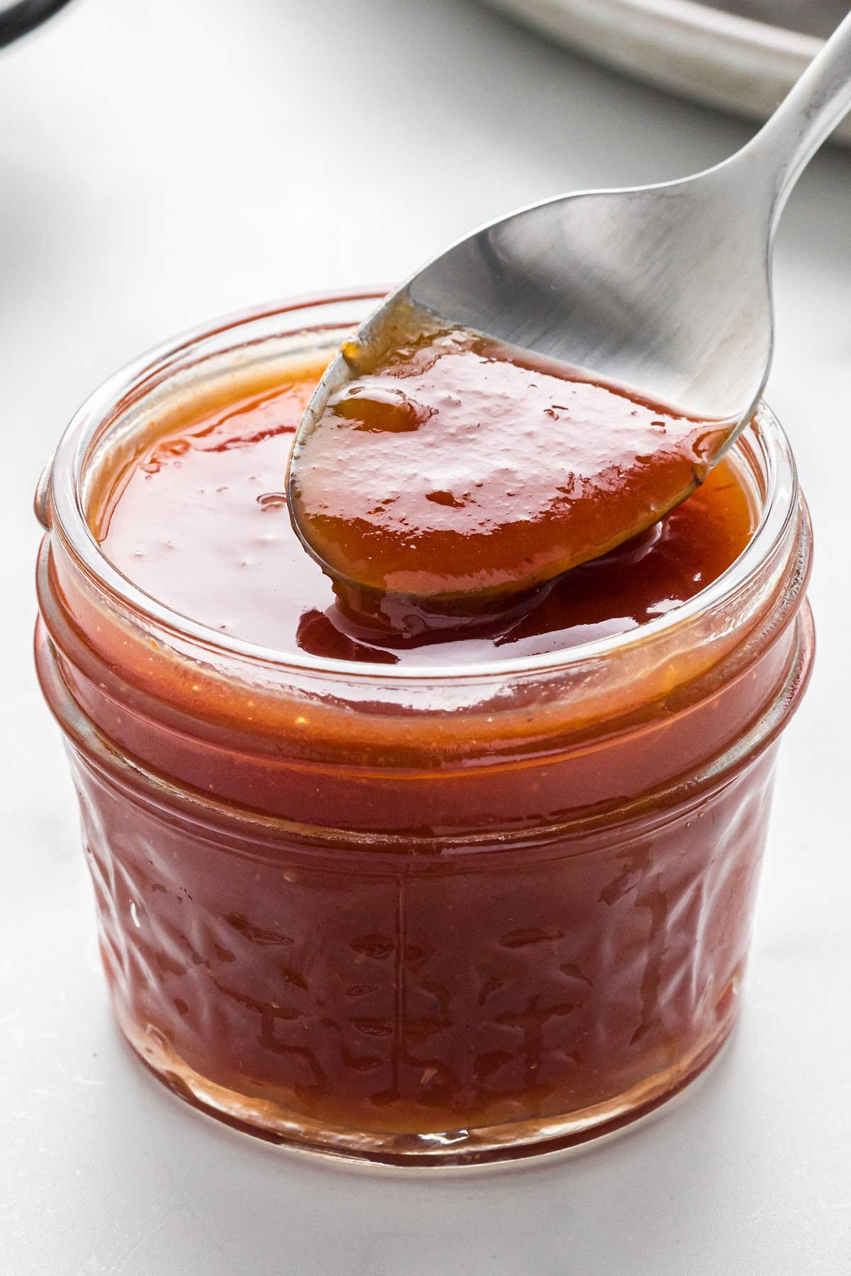 apricot barbecue sauce in a mason jar, with a spoon lifting some of the sauce.
