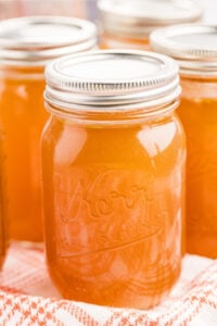 Multiple jars of chicken bone broth with metal lids, placed on a cloth.