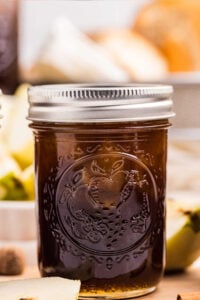 A close-up of a jar filled with pear preserves, sealed with a metal lid, with pears and spices in the background.