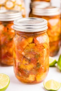 Several jars of pineapple mango salsa with metal lids, arranged closely together, featuring a fresh and colorful mix of diced fruits and vegetables.