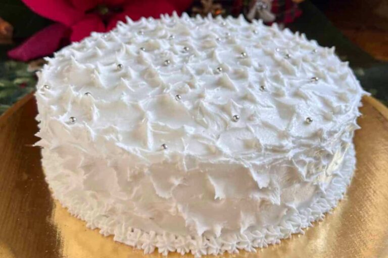 A traditional British fruit cake covered in royal icing with a textured, snowy appearance and silver beads.
