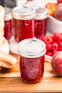 Mason jars filled with raspberry peach jam surrounded by fresh peaches and raspberries.