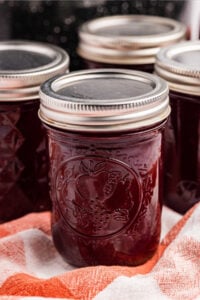 Close-up of sealed jars of raspberry syrup resting on a red and white cloth.